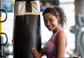 Portrait of a happy woman at the gym boxing and using a punching bag - sports training concepts